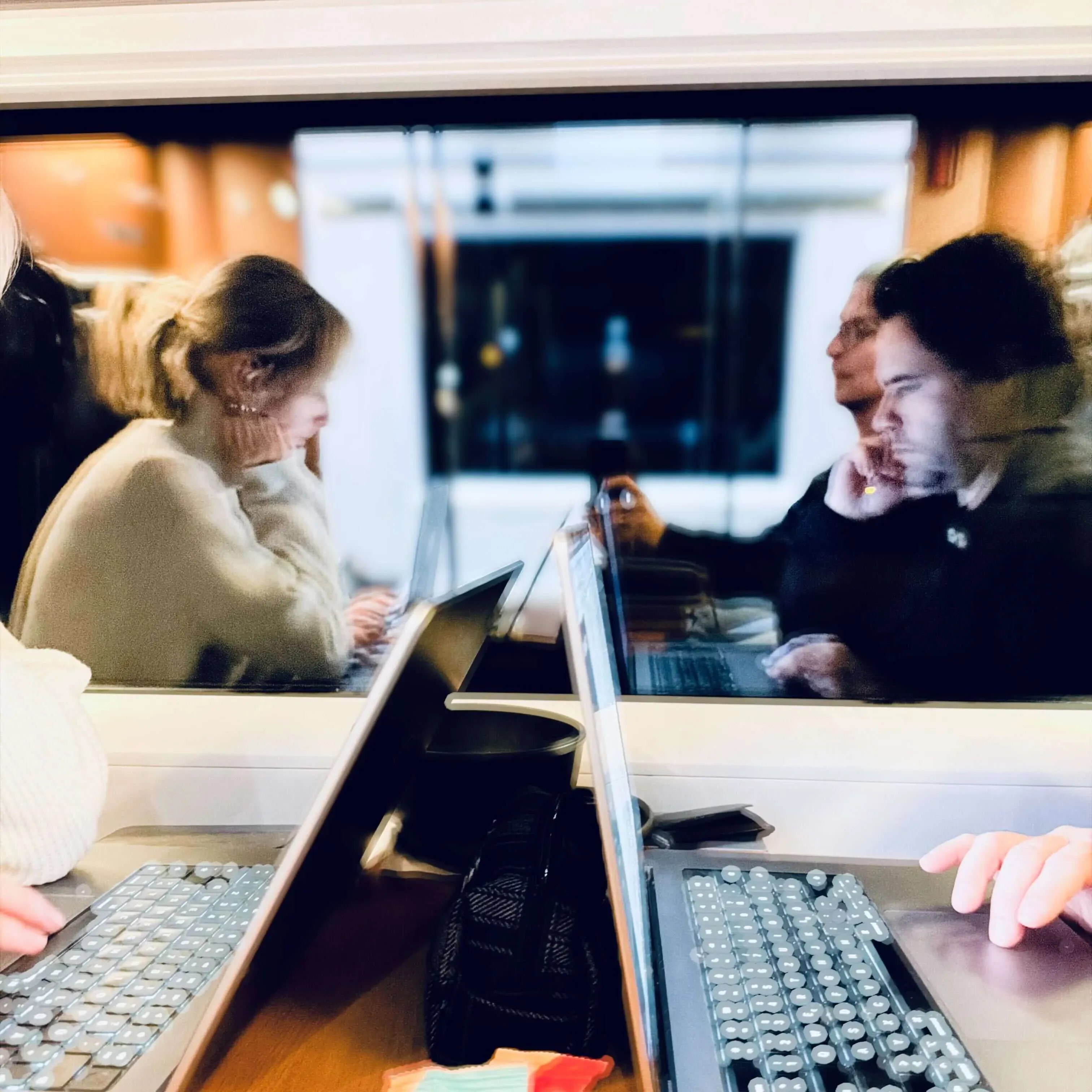 Zwei Laptops stehen nebeneinander, man sieht Mensch als Spiegelung in einem Fenster